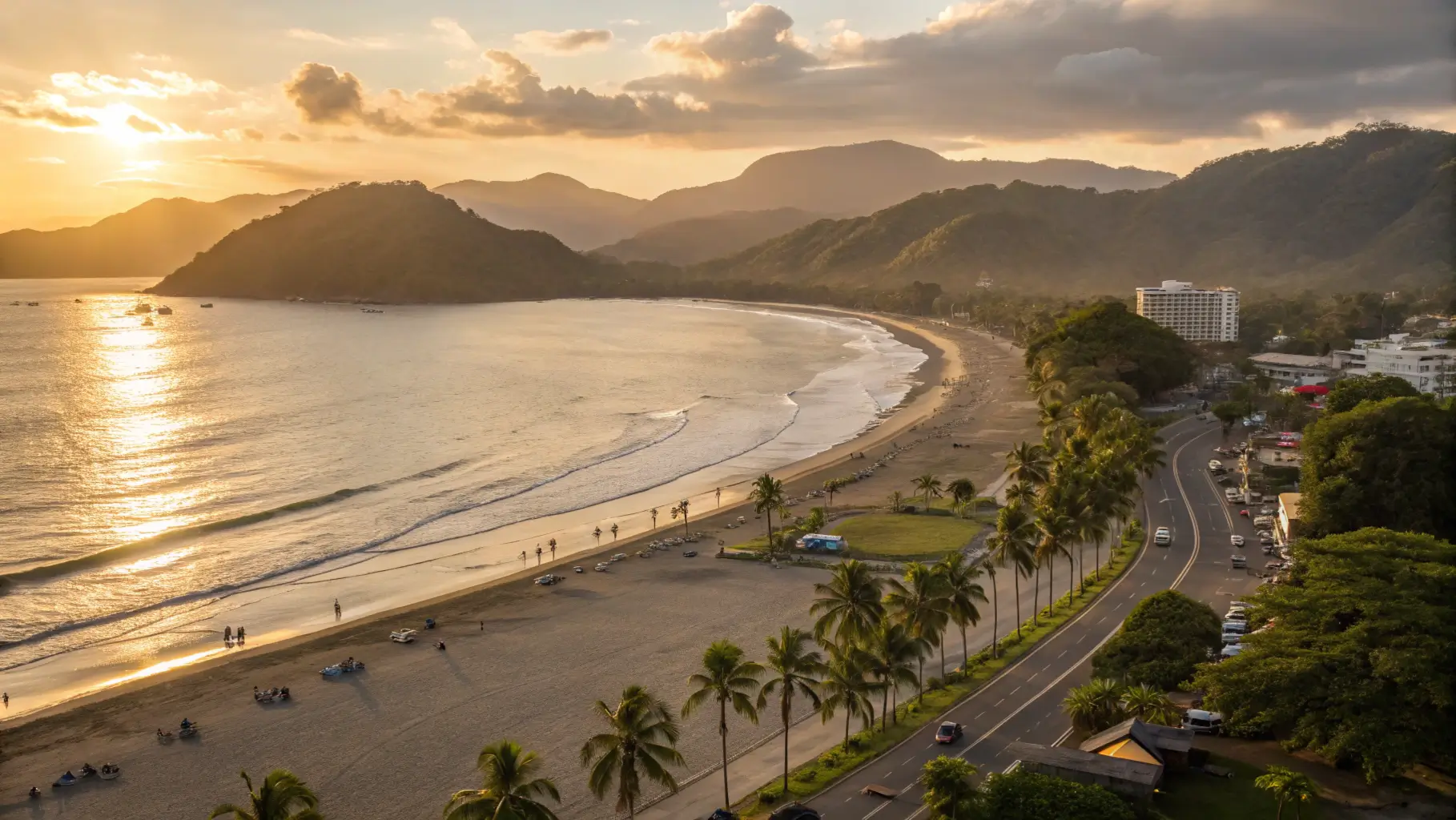 Panoramic view of Jaco Beach, Costa Rica at sunset with golden light illuminating the curved shoreline, palm trees, and mountains in the background.